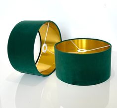 two green velvet lampshades with gold rims on white table top, one in the shape of a circle