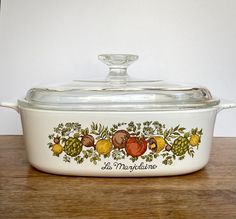 a casserole dish with fruit and vegetables painted on the side, sitting on a wooden table