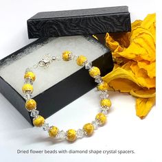 a bracelet with yellow beads sits next to a black box and flower on the table