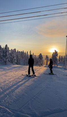 two people on skis in the snow near power lines and telephone poles at sunset