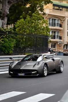 a silver sports car driving down the road in front of some tall buildings and trees