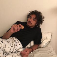 a young man laying in bed eating food