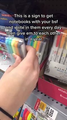 a person is holding pens in their hand and writing on the back of a book shelf