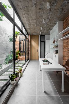 an empty room with large windows and a white table in the center is surrounded by plants