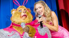 a woman in a pink dress is holding a microphone and standing next to a teddy bear