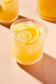 two glasses filled with drinks sitting on top of a table next to orange slices and lemon wedges