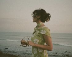 a woman standing on top of a beach next to the ocean holding a pair of scissors