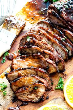 grilled meat on a cutting board with lemons and parsley