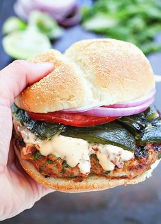 a hand holding a sandwich with meat, cheese and vegetables on it's bun