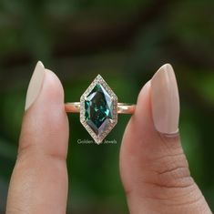 a woman's hand holding a ring with an emerald colored stone in the center