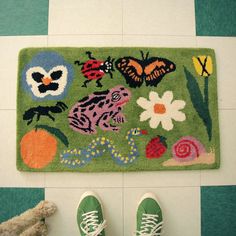 someone's feet are standing on the floor next to a rug with colorful animals and flowers