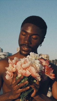 a shirtless man holding a bouquet of flowers in front of his face and chest