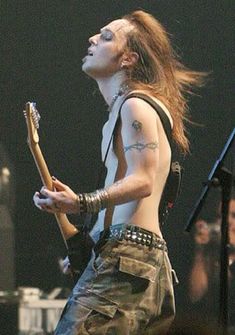 a man with long hair and piercings holding a guitar in front of a crowd