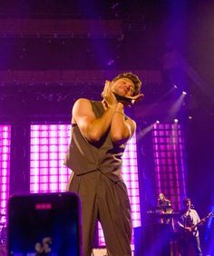 a man standing on top of a stage with his hands to his face as he sings