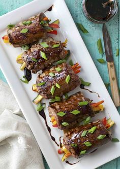 some meat is sitting on a white plate with sauce and green onions next to it