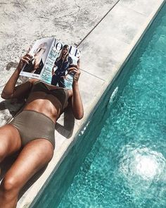 a woman laying next to a swimming pool reading a magazine