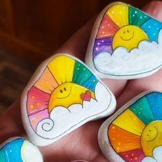 three painted rocks in the shape of sun and rainbows with clouds, stars and hearts