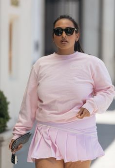 a woman in a pink outfit is walking down the street with her hand on her hip