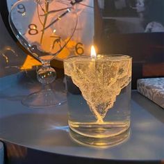 a lit candle sitting on top of a table next to a glass vase filled with water