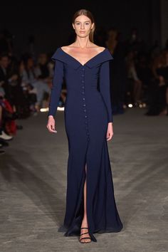 a model walks the runway in a blue gown with an asymmetrical neckline