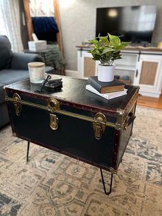 an old trunk is sitting on the floor in front of a coffee table with books and a potted plant