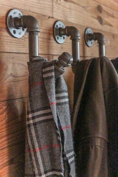 three coats hanging from hooks on a wooden wall next to two towel racks and one coat rack