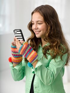 a woman holding up a cell phone wearing knitted mitts and a green shirt