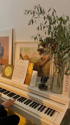 a woman sitting at a piano playing the music on it's own side with pictures and plants in front of her