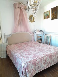 a bed with pink bedspread and chandelier hanging from the ceiling in a bedroom