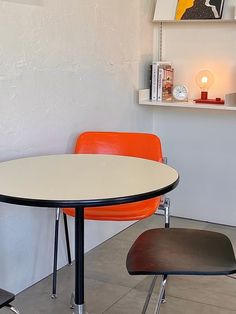 an orange chair sits in front of a white table with two black chairs on it