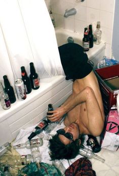 a man sitting on the floor in front of a bathtub full of beer bottles