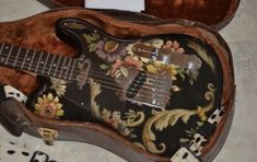 an electric guitar is laying on the floor next to a case with flowers and leaves painted on it