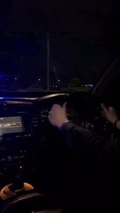 two people in a car at night with their hands on the steering wheel and lights on