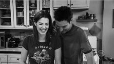 a man and woman are standing in the kitchen preparing food together, smiling at each other