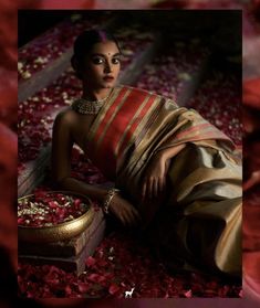 a woman sitting on the ground surrounded by rose petals in a sari and jewelry