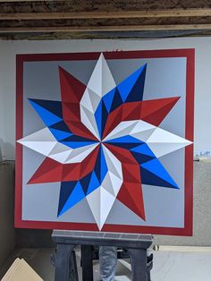 a man standing in front of a large red, white and blue star quilt on a easel