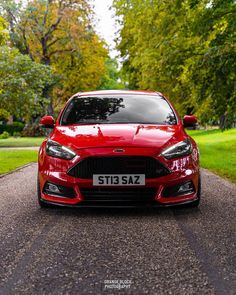 a red car parked on the side of a road next to some grass and trees