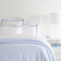 a white bed with blue and white comforter in a bedroom next to a lamp