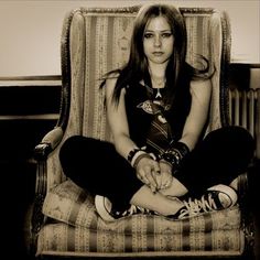 a young woman sitting in a chair with her hands on her knees and looking at the camera