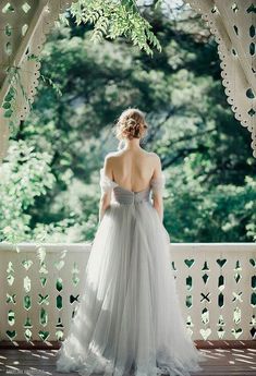 a woman in a wedding dress standing on a porch looking out at the trees and greenery