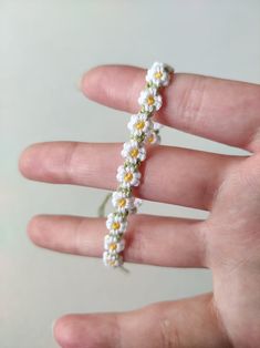 a hand holding a tiny white and yellow flower beaded bracelet