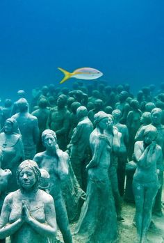 a group of statues under water with a fish in the background