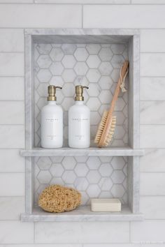 two bathroom shelves with soap, toothbrush and scrub on them in white marble tiles