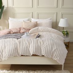 a white bed with pillows and blankets on it in a room next to a plant