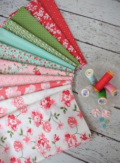 a bunch of different types of fabric on a wooden table with spools of thread