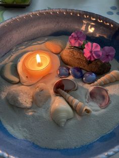 a bowl filled with sand and seashells next to a lit candle on top of it