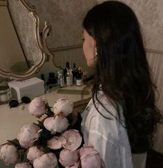 a woman standing in front of a mirror holding a bunch of pink tulips