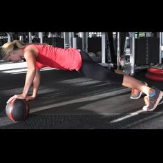 a woman is doing push ups with a medicine ball in the middle of a gym