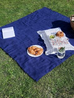 a picnic blanket with croissants and drinks on it sitting in the grass