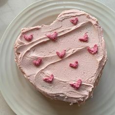 a heart shaped cake on a plate with pink frosting and hearts around the edges